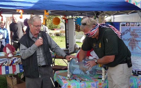 Blindfolded Sheriff Rob Nou picks the winning ticket for the Hawaii vacation raffle winner while Frank Penwell stands ready to announce the winner. The drawing was held at the end of the Pioneer Festival.