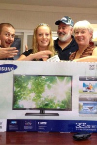Randy Lindsey (2nd from right), Mike Scott (left) and Lorie Narum (right) of the local Zito Media FridayHarbor office, hand off the 32 inch HD color TV to  winner Jenna Avery.