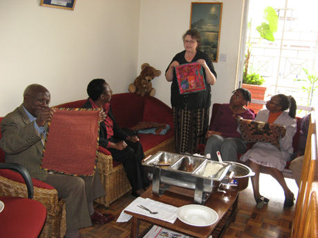 From Jill: "Mom sharing her plans with the Oasis Africa staff before we set out to Mashaka. Gladys is on the sofa and Gershon is admiring one of Mom's quilts."